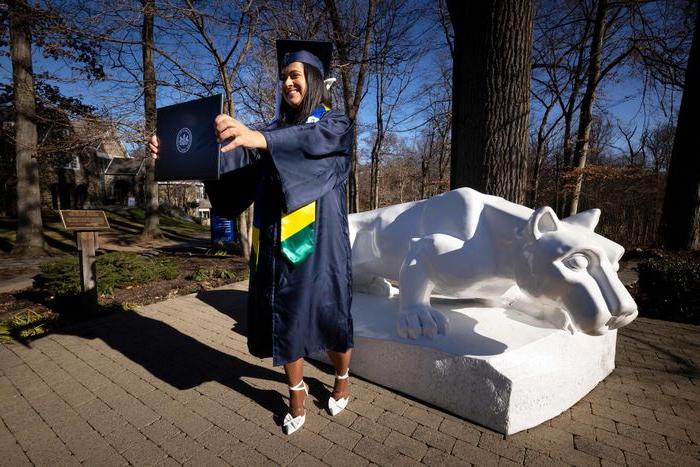 Student holding diploma in front of Lion Shrine 